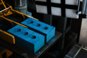 an image of two blue bricks having just been formed by a machine. There are orange arms which have held the bricks and are now releasing them.