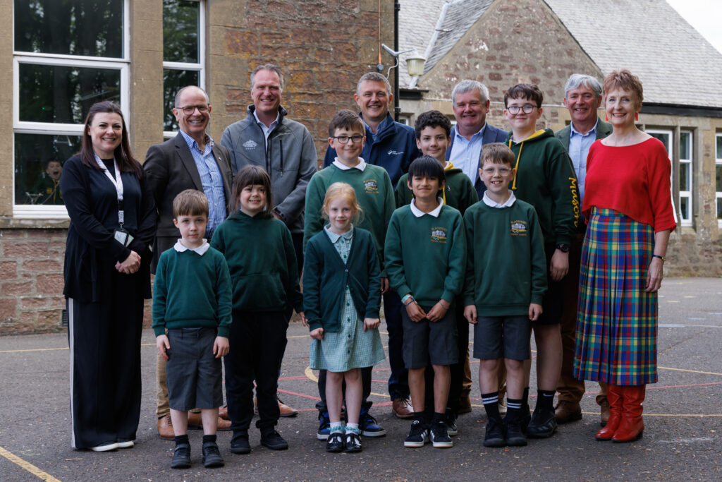 A group of school children outside their school building with teachers and local leaders