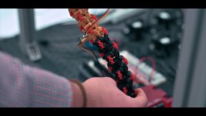 Close-up of hands holding a black segmented robotic tentacle with red connectors in a laboratory setting, demonstrating the flexible soft manipulator technology developed by the National Robotarium for underwater inspection applications.