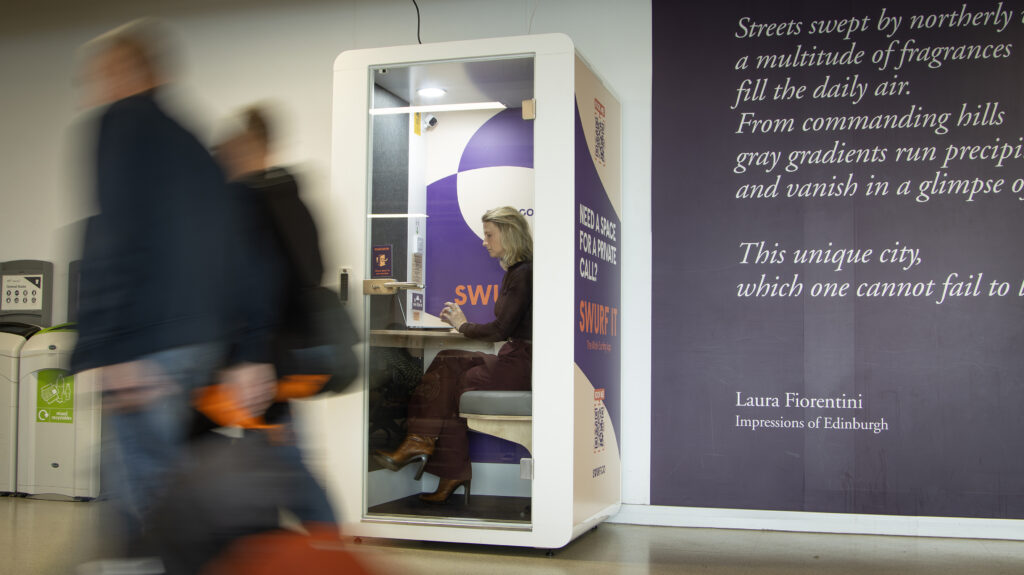SWURF private meeting pod in use at Edinburgh location showing businesswoman taking video call in soundproof workspace while commuters pass by