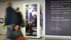 SWURF private meeting pod in use at Edinburgh location showing businesswoman taking video call in soundproof workspace while commuters pass by