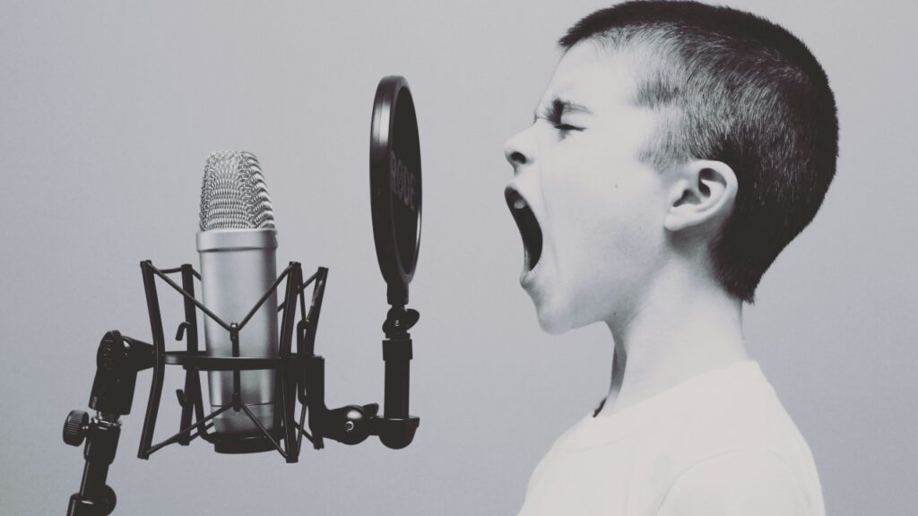 Black and white photo of a young boy shouting into a studio microphone with a pop filter – Hot Tin Roof PR agency image by Jason Roswell