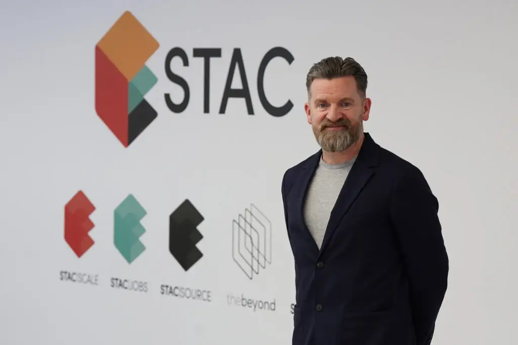 Paul Wilson Paul Wilson, CEO and Co-Founder of STAC, stands in front of the STAC logo and brand wall at thebeyond technology hub in Glasgow, featuring the STAC Scale, STAC Jobs, STAC Source and thebeyond sub-brand logos.