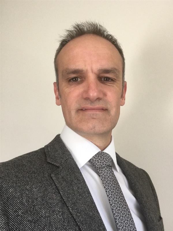 Headshot of Stephen Wood, Head of Siemens eMobility UK, wearing a grey blazer, white shirt, and patterned grey tie, photographed against a plain light background.