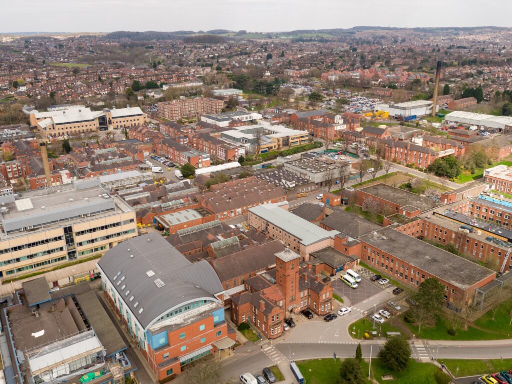 Aerial view of the Nottingham City Hospital site showing the extensive red-brick campus with multiple buildings, car parks, and surrounding residential Nottingham cityscape.