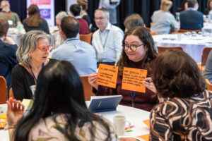 Participants at the Edinburgh Data and AI Exchange Stakeholder Assembly at Edinburgh Futures Institute discussing AI infrastructure investment themes using orange post-it notes, including ideas on core stable investment, mixed funding models, and the need for better storytelling around data centres and innovation ecosystems, contributing to the evidence base for the Governing the Future report