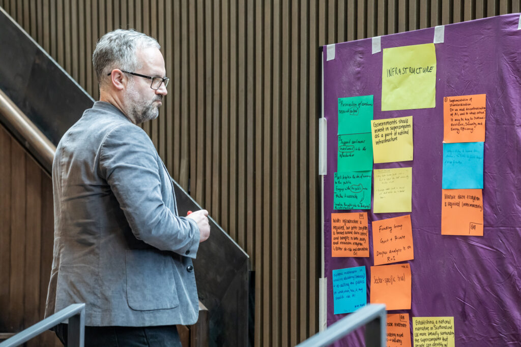Professor Oliver Escobar, Chair of Public Policy and Democratic Innovation at the University of Edinburgh and designer of the Stakeholder Assembly, reviewing participant post-it notes on an infrastructure theme board at the Edinburgh Data and AI Exchange event held at Edinburgh Futures Institute in March 2026, part of structured deliberative methodology informing AI governance recommendations