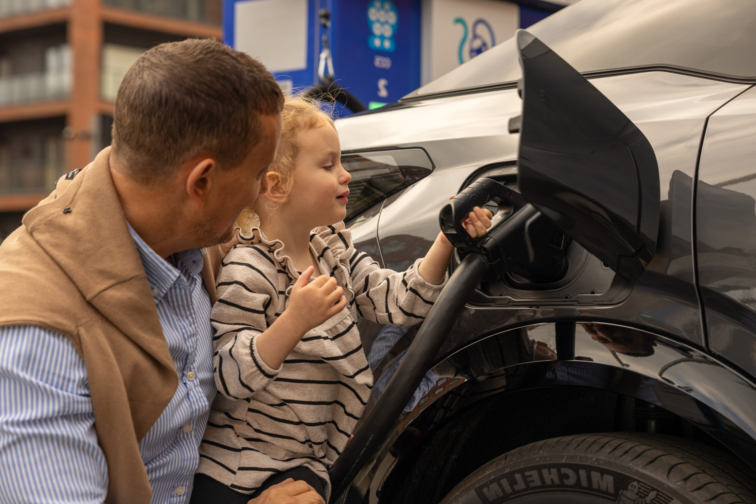 Young girl helps her father plug in an EV at a Source charging hub
