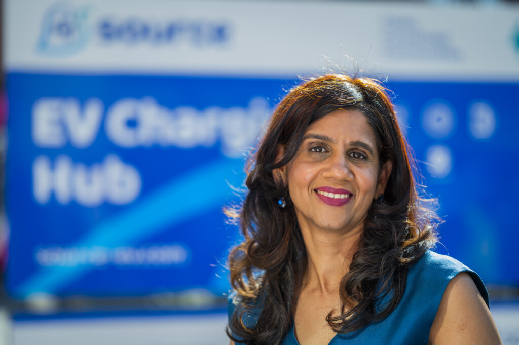 Deepa Chandrasekaran, Managing Director of Source EV, smiles in front of an EV Charging Hub sign. PR Agency. Source charge point operator