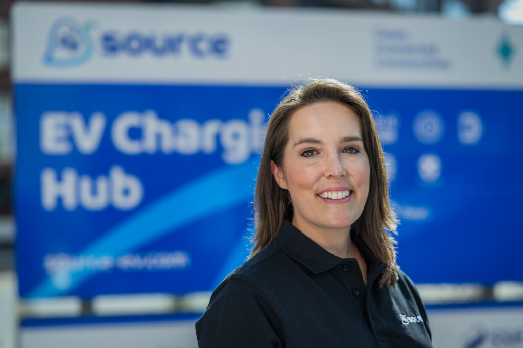 Alice Aprile-Smith, Head of Partnerships and Business Development at Source, smiling in front of a Source EV Charging Hub sign