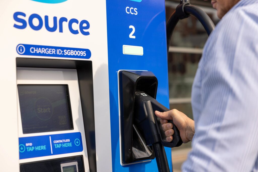 Driver lifting a CCS connector from a Source ultra-rapid EV charger with touchscreen, RFID and contactless payment panel