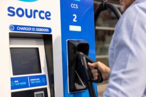 Driver lifting a CCS connector from a Source ultra-rapid EV charger with touchscreen, RFID and contactless payment panel